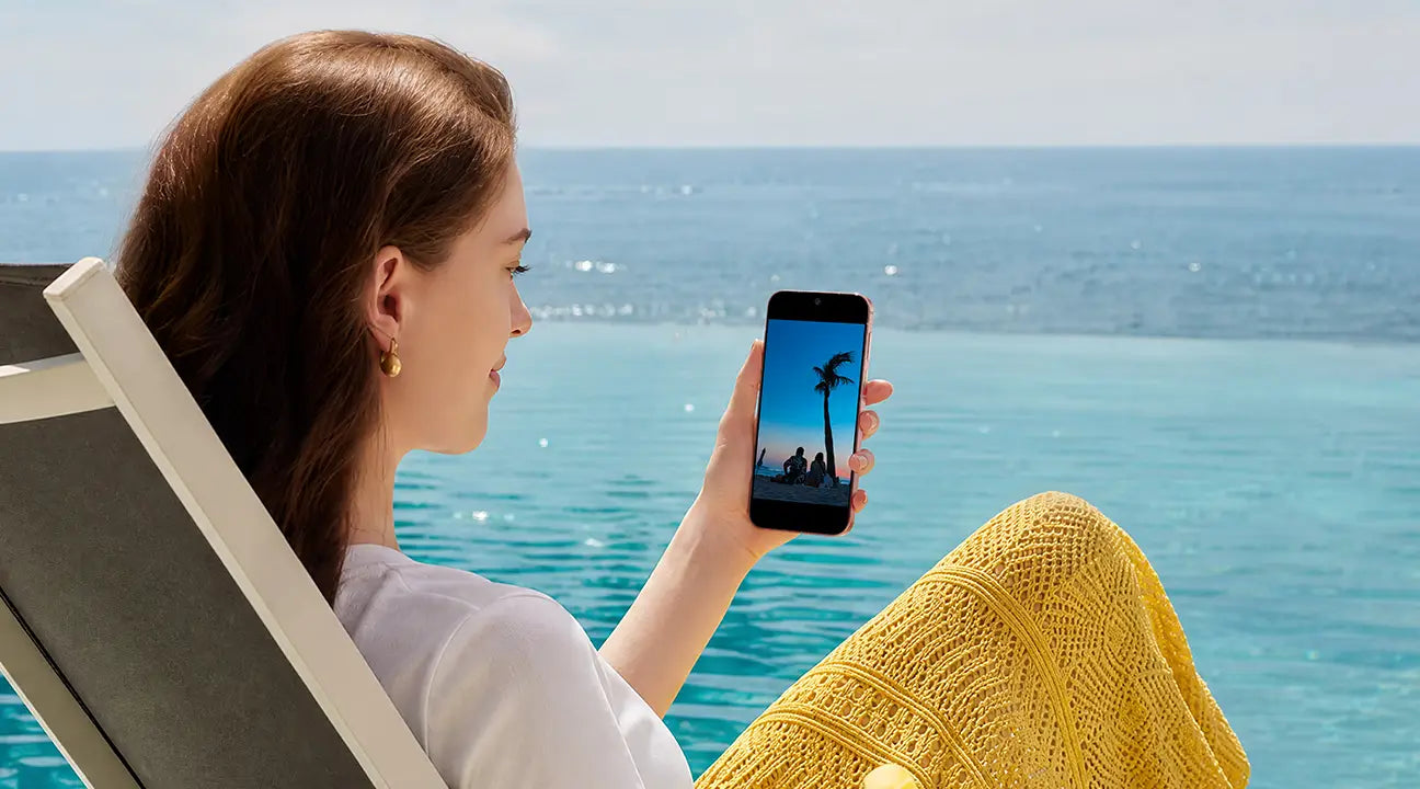 A female is sitting by the seaside with HUAWEI Pura 90s Pro in hand, show the 6000mah long battery life